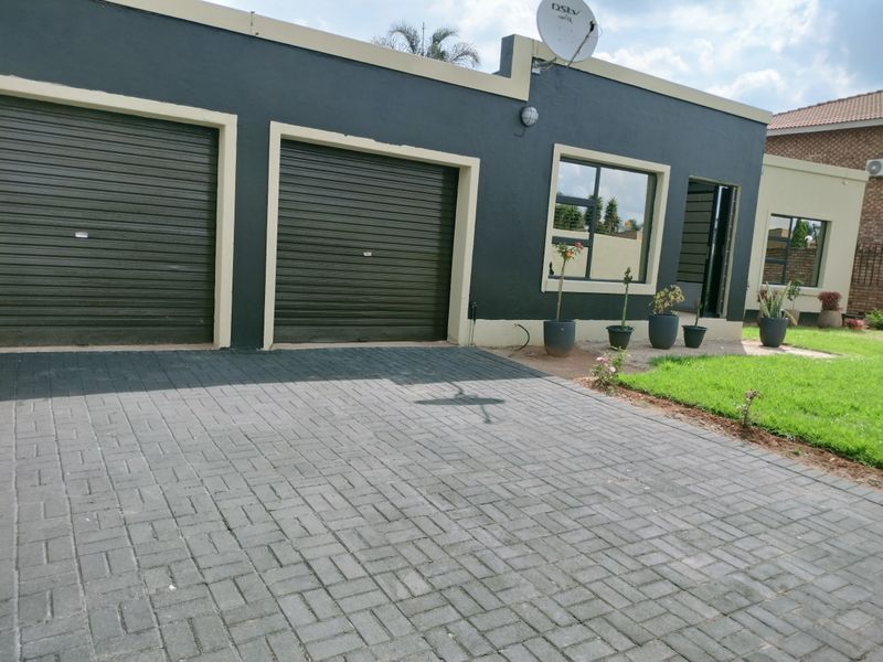 Exterior view of the property featuring a double garage with roller doors, paved driveway, and a well-maintained front garden area.