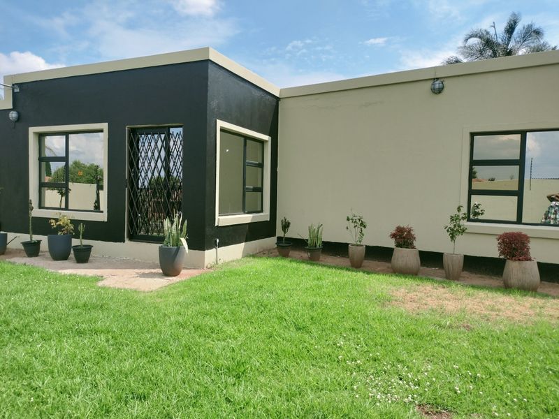 Rear exterior view of the house featuring a manicured lawn, modern dark and light painted facade, and secure metal security gate.
