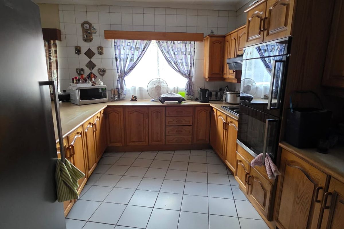 A functional kitchen featuring traditional timber cabinetry, tiled splashbacks, tiled flooring, and built-in oven and cooktop appliances.