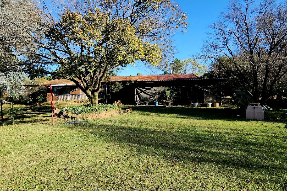 A view of the rear exterior of the property featuring a spacious lawn, mature trees, and a covered patio area.