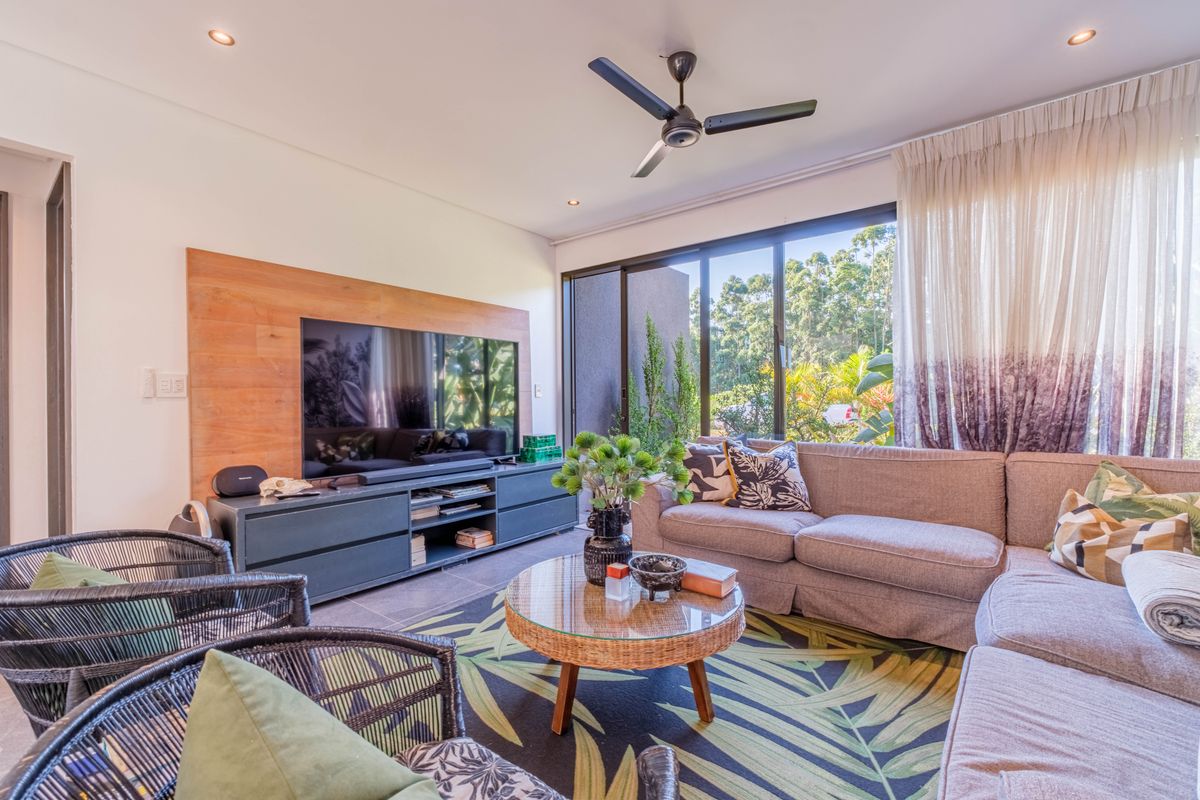 A bright and modern living room featuring large sliding glass doors, a built-in wooden media wall, and a ceiling fan.
