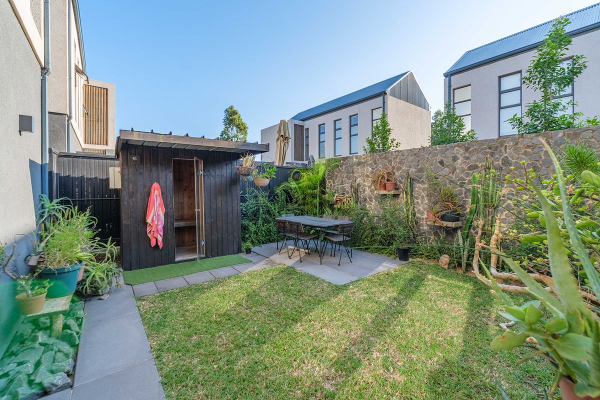 A private rear garden featuring a manicured lawn, stone-clad boundary wall, paved patio area, and a detached timber sauna structure.