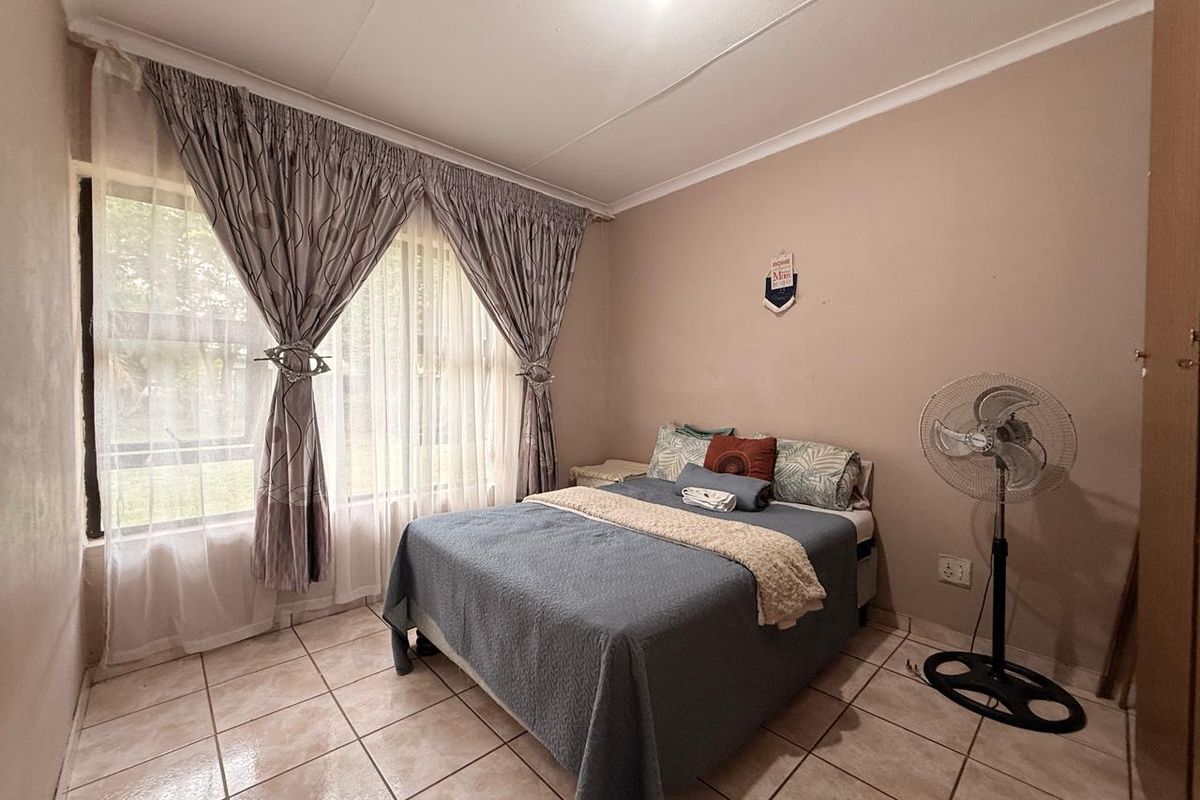 A bedroom featuring tiled flooring, large windows with curtains, and neutral wall finishes.