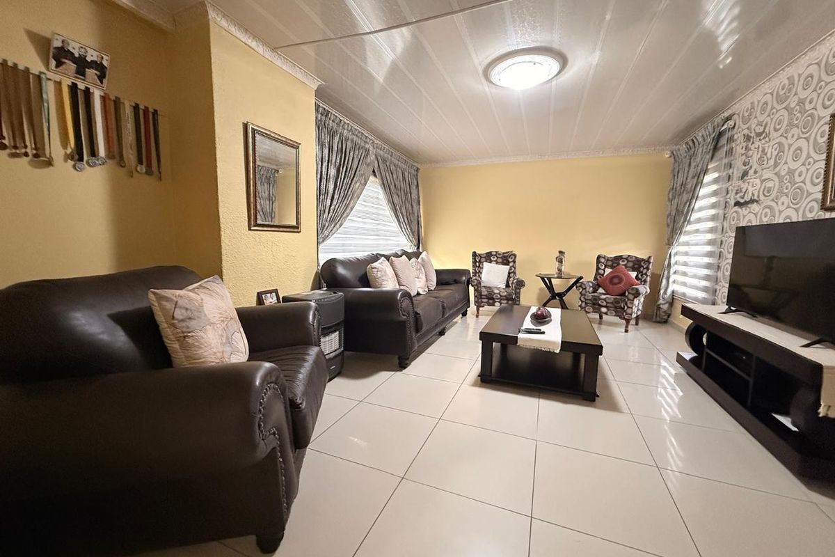 A spacious living room featuring large format floor tiles, decorative ceiling cornices, and dual-aspect windows with fitted blinds.