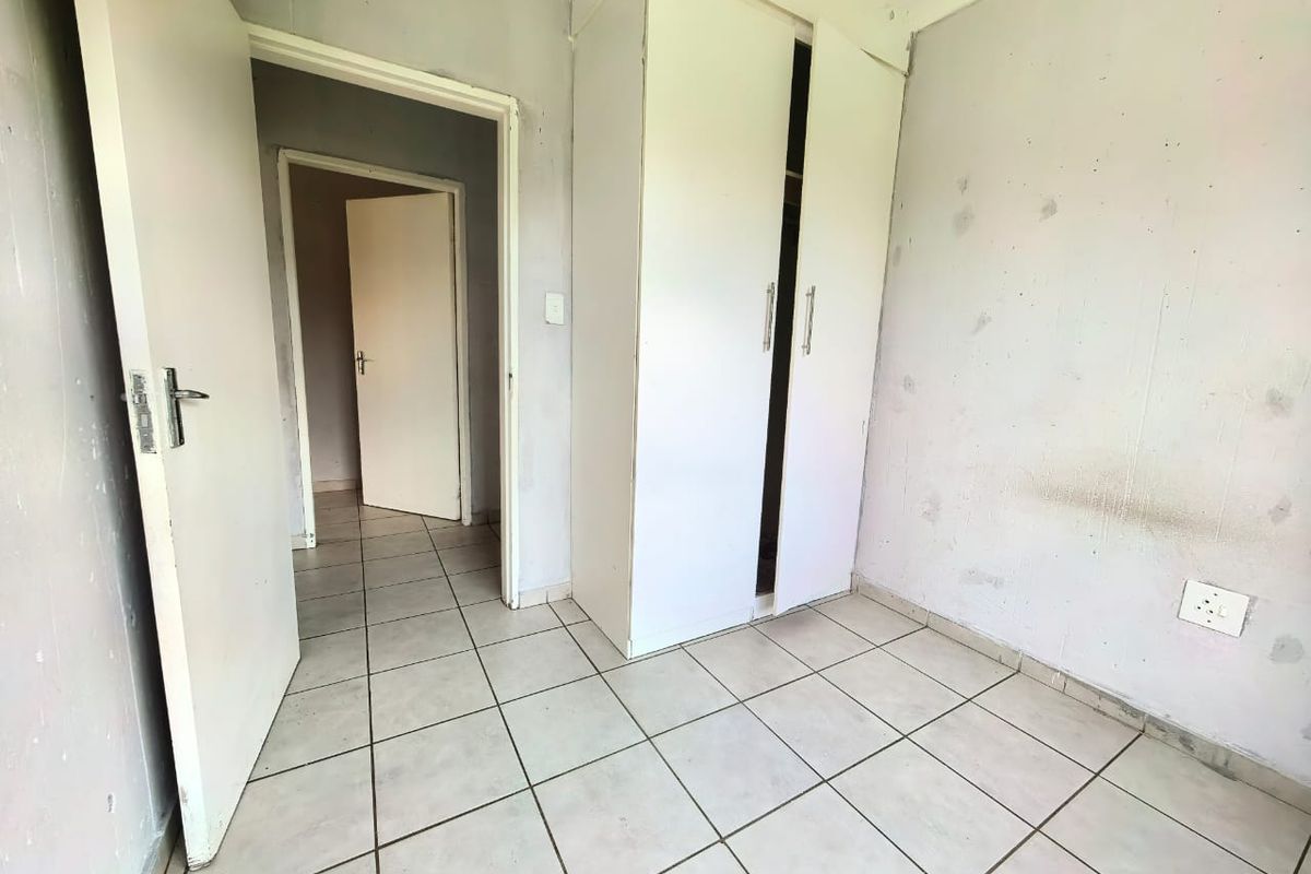 A small bedroom featuring tiled flooring and a built-in wardrobe, requiring cosmetic updates to the wall finishes.