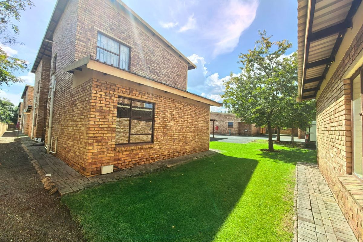 Exterior view of the townhouse featuring face-brick facade, paved walkways, and a well-maintained lawn area.