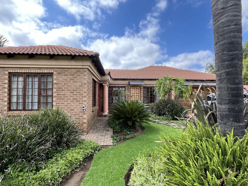 A well-maintained face-brick exterior of a small holding property featuring a terracotta tiled roof, landscaped garden, and paved walkway.