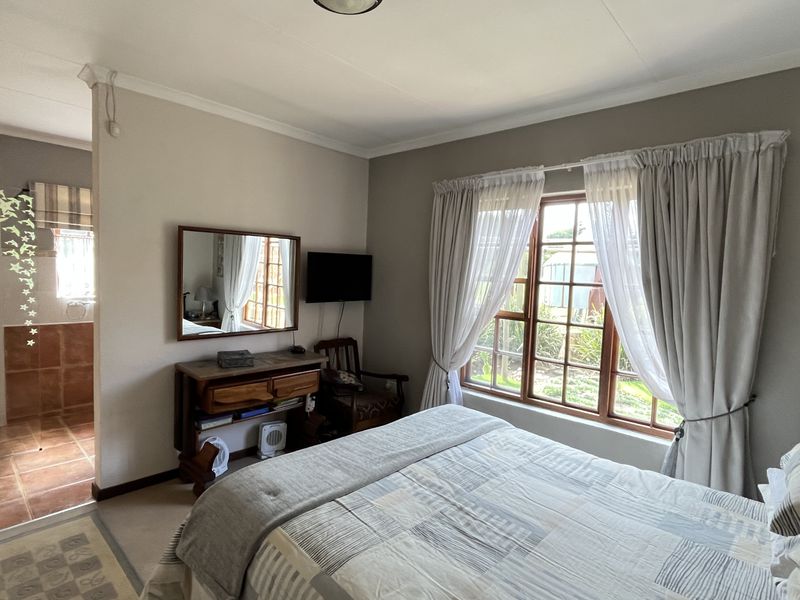 A bedroom featuring a wooden window frame, built-in cupboards, and an open-plan en-suite bathroom with tiled flooring.