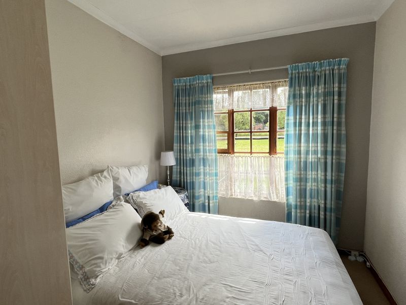 A cozy bedroom featuring a window with garden views, neutral wall finishes, and built-in cupboard space.