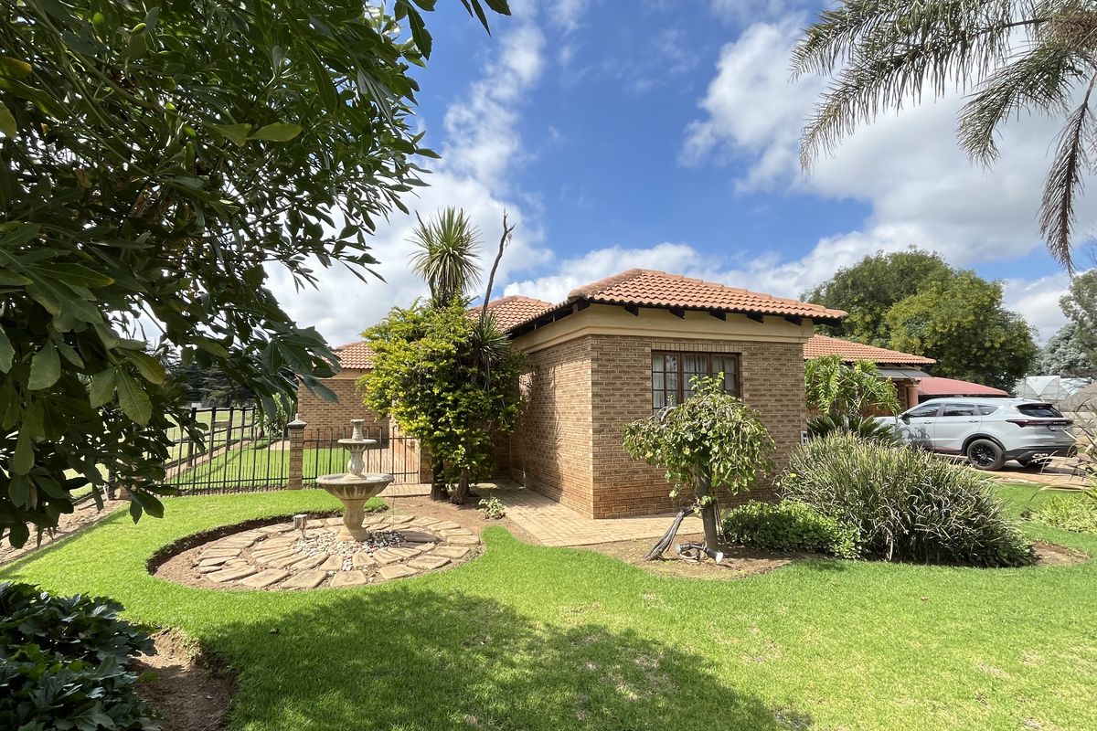 A well-maintained face-brick exterior of the small holding, featuring a tiled roof, landscaped garden, and a decorative stone-paved water feature.