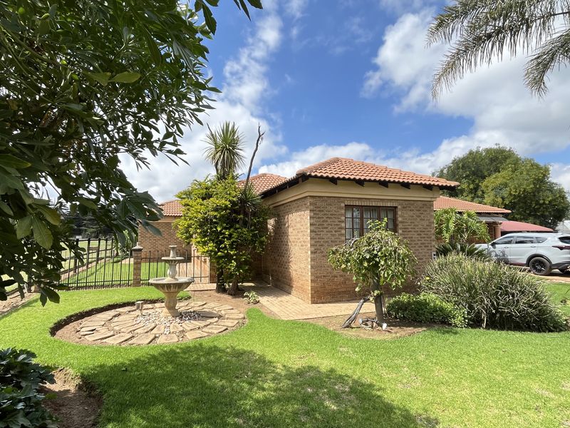 A well-maintained face-brick exterior of the small holding, featuring a tiled roof, landscaped garden, and a decorative stone-paved water feature.