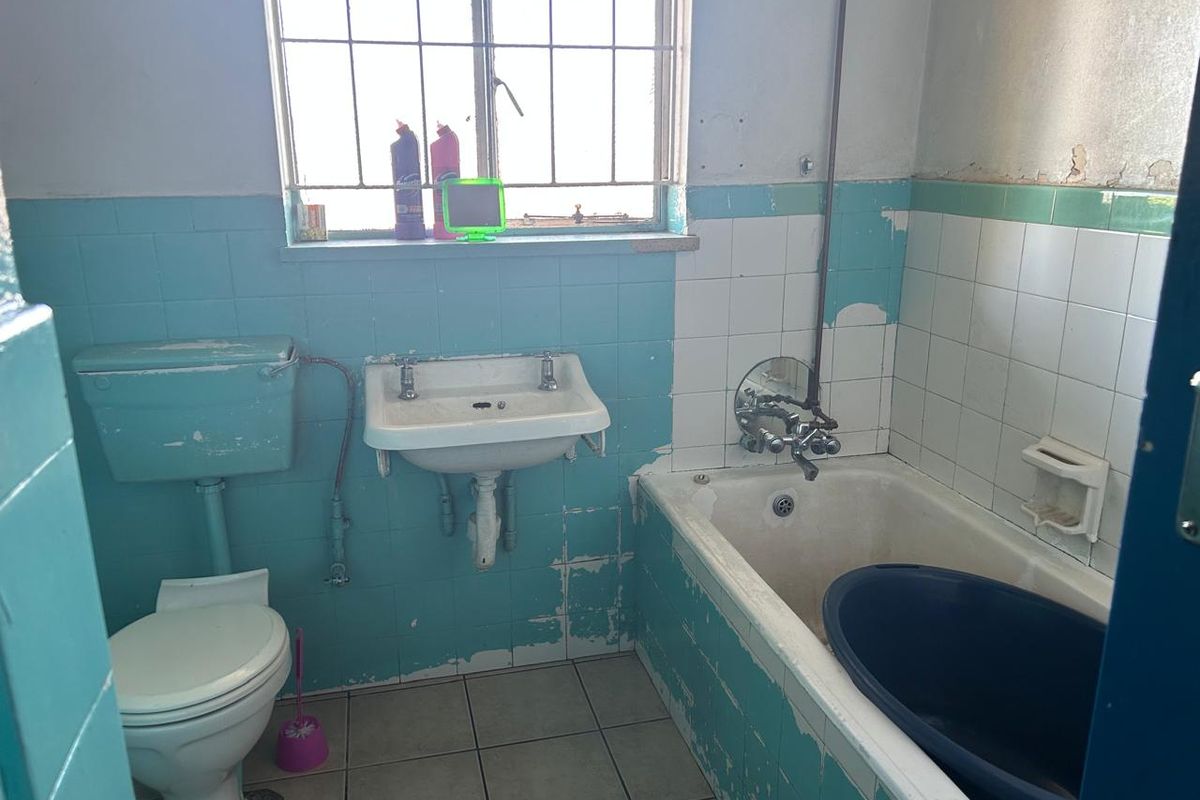 A dated bathroom featuring a standard bathtub, wall-mounted basin, and toilet, requiring significant renovation and modernization of finishes and fixtures.