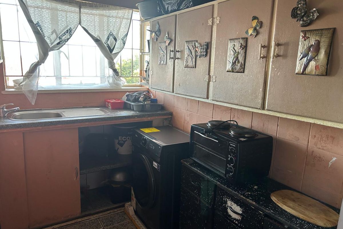 A compact kitchen featuring dated cabinetry, tiled splashbacks, a stainless steel sink, and space for a washing machine under the counter.