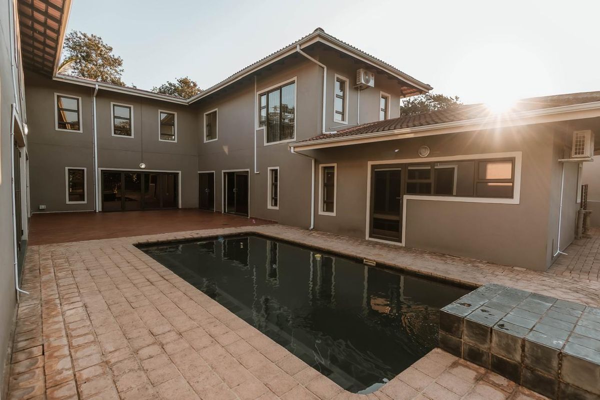 A spacious rear exterior view featuring a swimming pool, paved patio area, and a multi-level house with modern finishes and integrated air conditioning units.