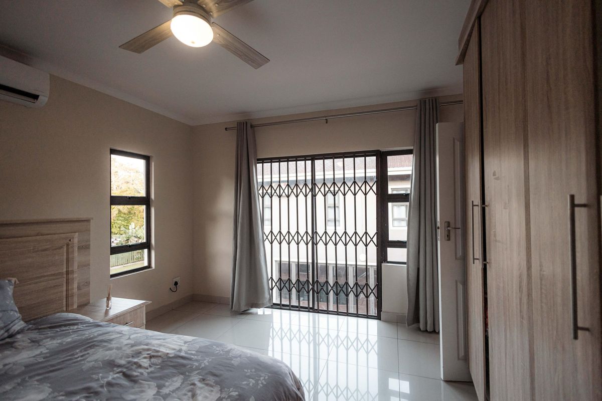 A well-maintained bedroom featuring tiled flooring, built-in wooden cupboards, a ceiling fan, and an air conditioning unit with access to a balcony.