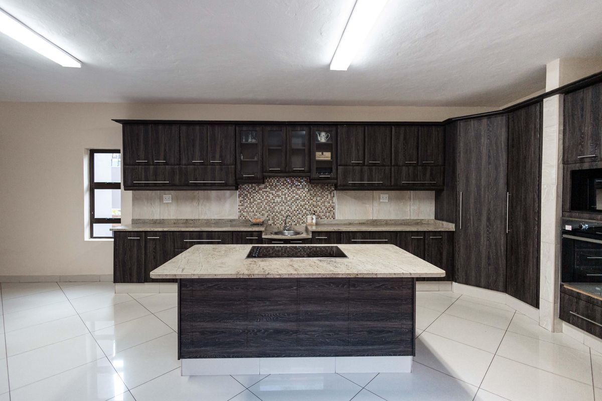 Spacious kitchen featuring dark wood cabinetry, stone countertops, a central island with a built-in cooktop, and polished tile flooring.