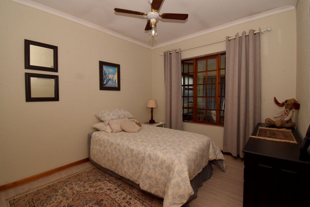A cozy bedroom featuring a ceiling fan, timber-framed window, and neutral wall finishes, providing a comfortable and functional sleeping space.