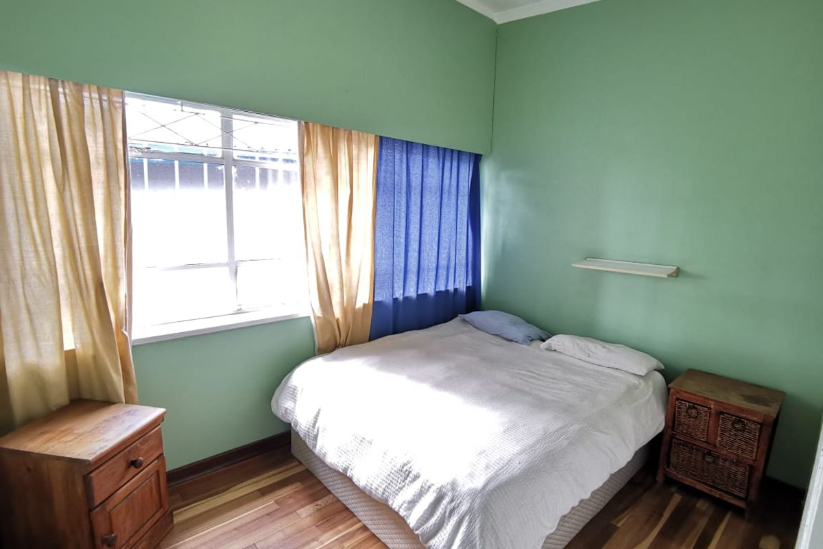 A bedroom featuring timber flooring, large windows with curtain fixtures, and a wall-mounted shelf.