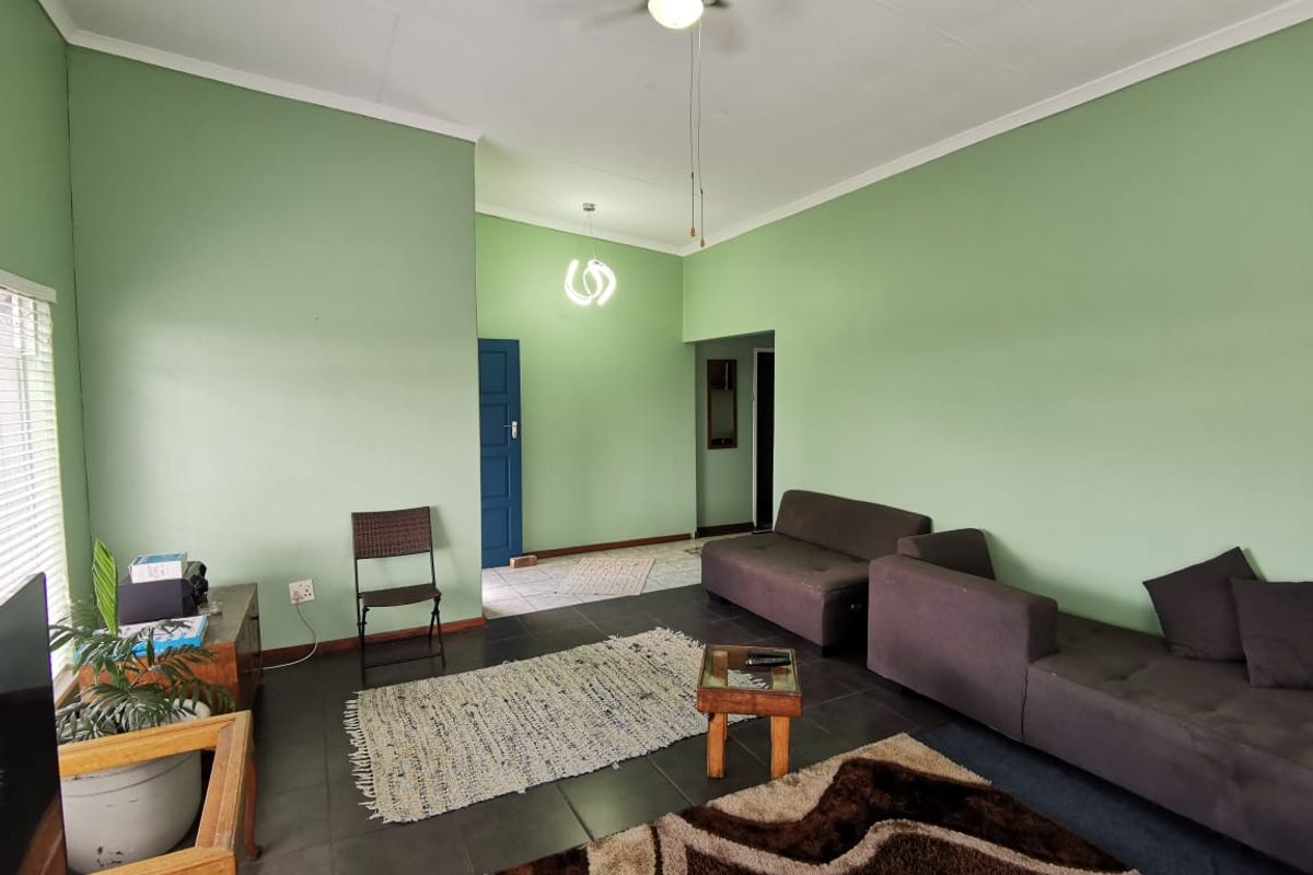 A spacious living room featuring dark floor tiles, light green walls, and a ceiling fan, offering a functional layout for comfortable family living.