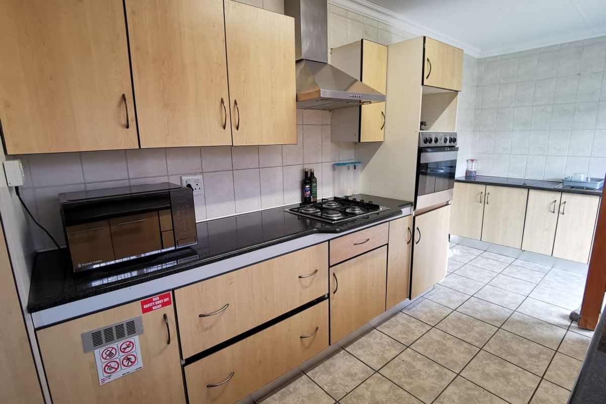 A functional kitchen featuring light wood-tone cabinetry, black granite countertops, a built-in oven, gas hob, and stainless steel extractor fan.