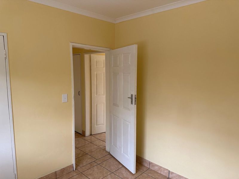 An empty bedroom featuring tiled flooring, neutral yellow walls, and classic panelled interior doors, offering a blank canvas for personalization.