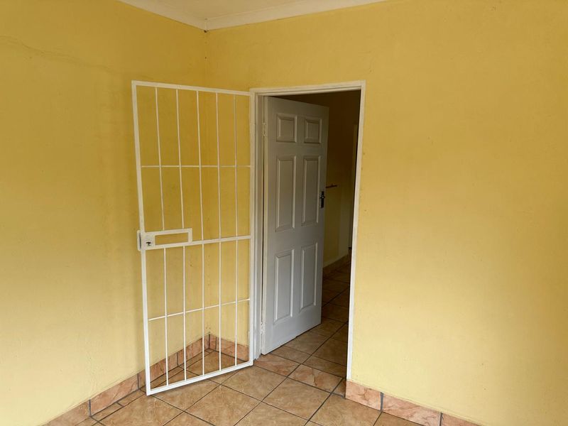 An empty bedroom featuring tiled flooring, a white internal door, and a fitted security gate, finished with yellow wall paint.
