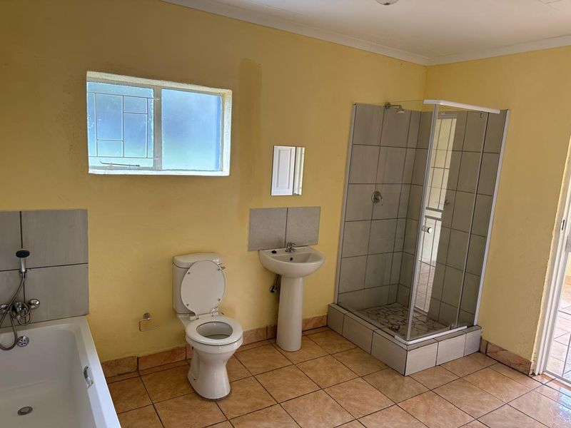 A functional bathroom featuring a shower enclosure, bathtub, pedestal basin, and toilet with tiled flooring and neutral wall finishes.