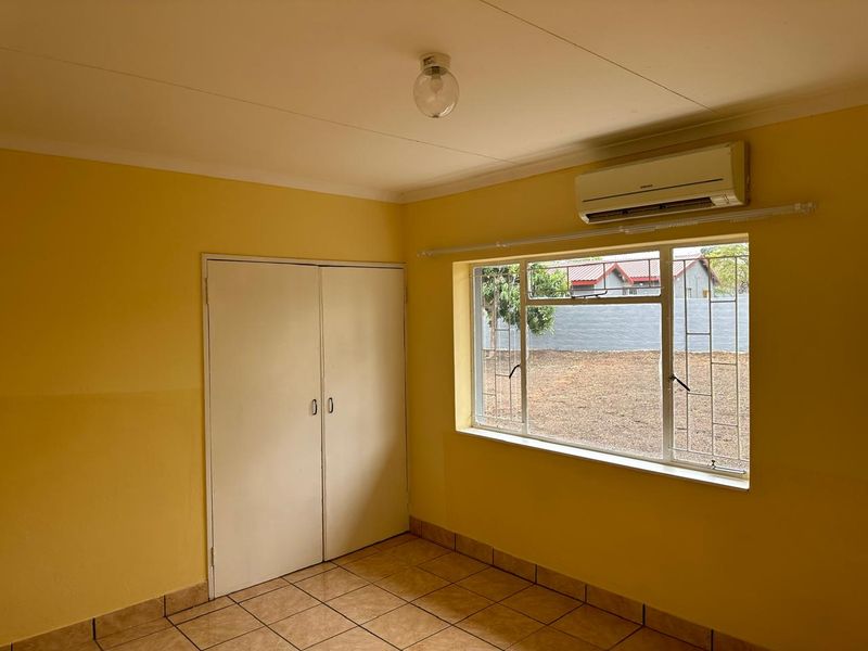 An empty bedroom featuring tiled flooring, a built-in cupboard, and an air conditioning unit, with a window overlooking the exterior yard.