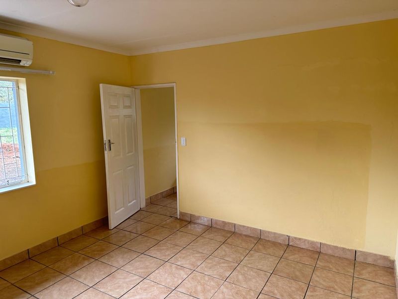 An empty bedroom featuring tiled flooring, an installed air conditioning unit, and security bars on the window.
