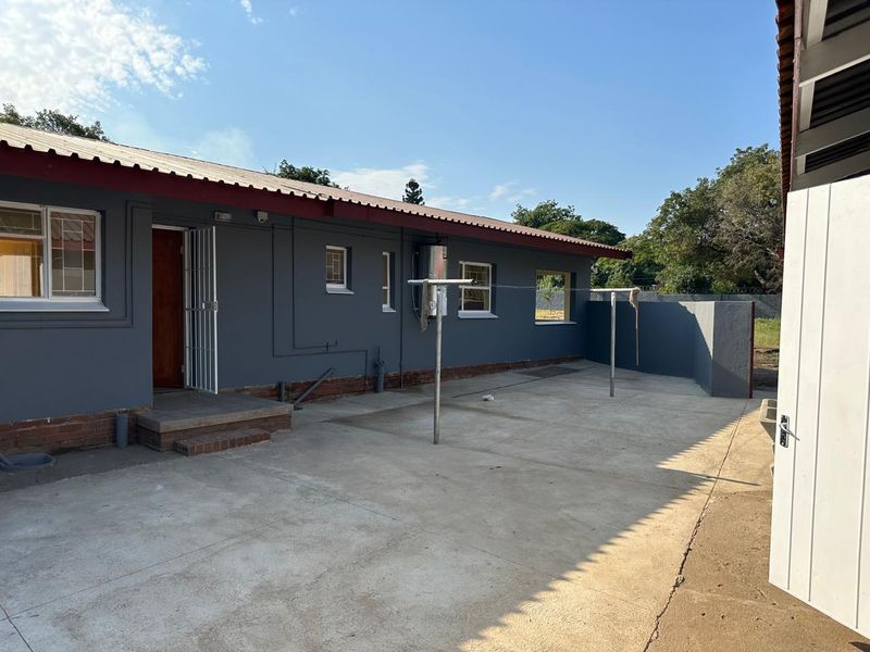 Rear exterior view of the house featuring a concrete patio area, security gate, and external geyser installation.