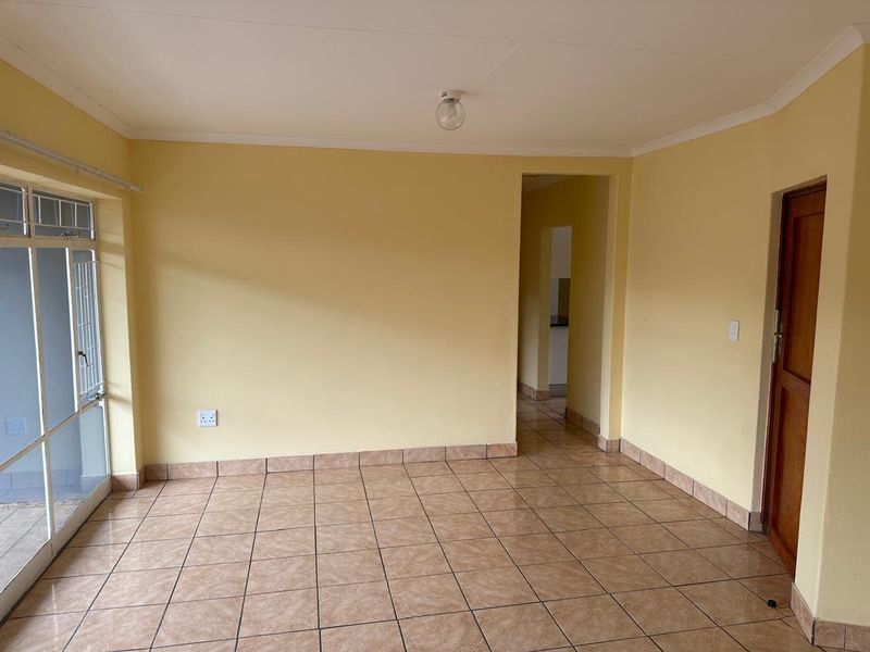 A bright, empty living room featuring tiled flooring, neutral walls, and a sliding glass door providing access to the exterior.