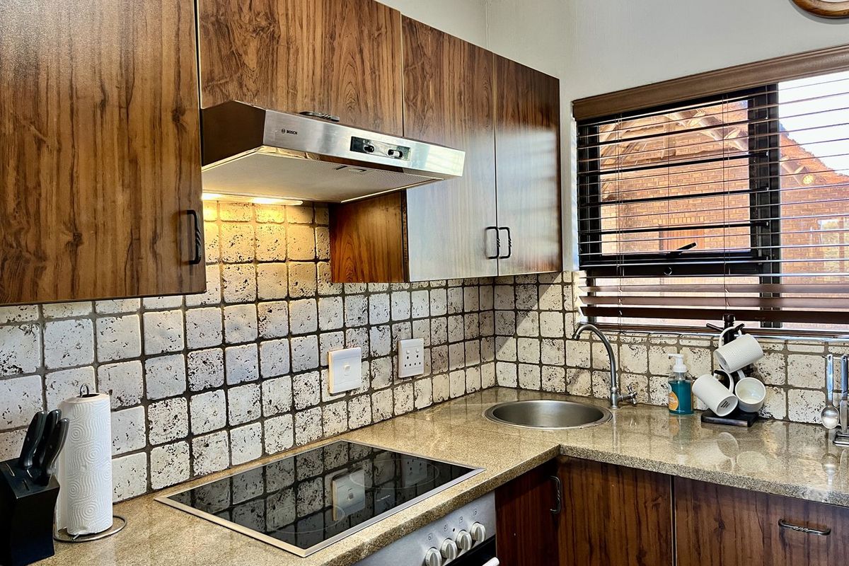 Compact kitchen featuring wood-grain cabinetry, granite countertops, a built-in electric hob, extractor fan, and a stainless steel sink.