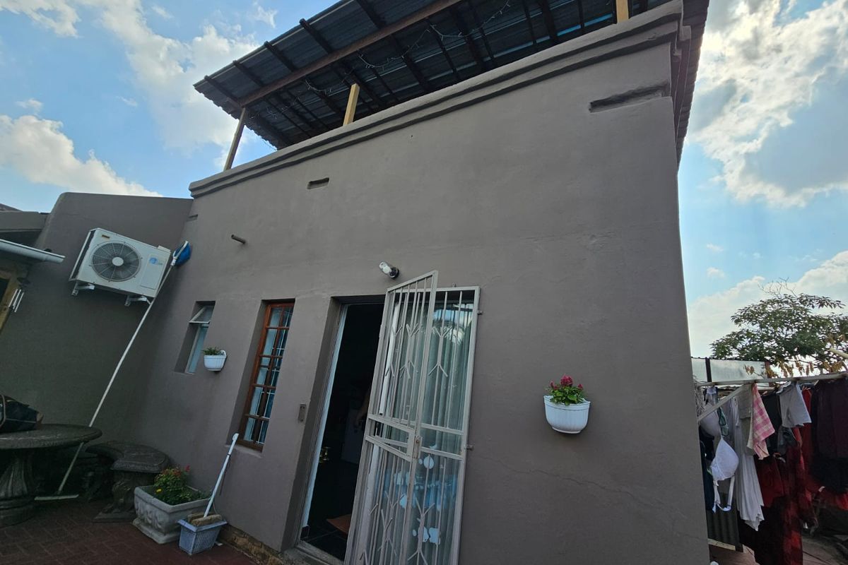Rear exterior view of the property featuring a paved patio area, security gate, and an external air conditioning unit.