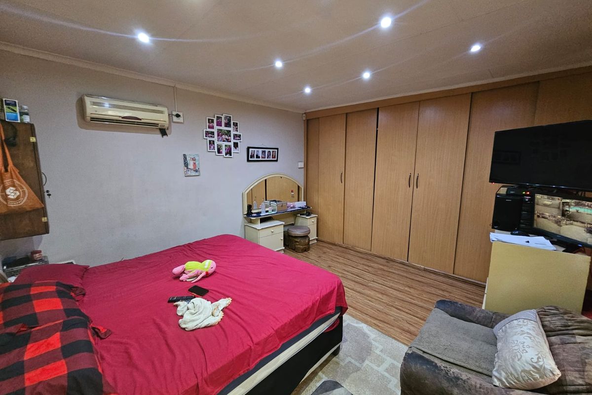 A spacious bedroom featuring built-in wooden wardrobes, laminate flooring, recessed ceiling downlights, and a wall-mounted air conditioning unit.
