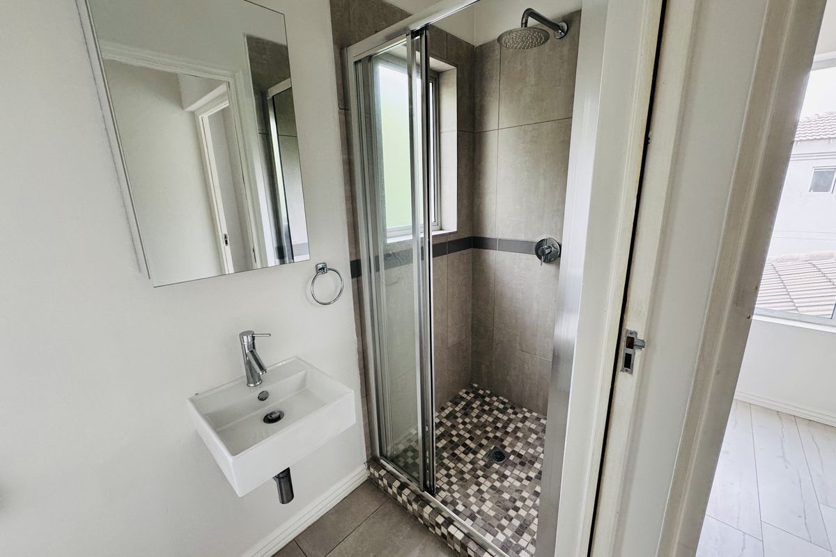 A clean, modern bathroom featuring a wall-mounted basin, a glass-enclosed shower with mosaic floor tiling, and a wall-mounted mirror.