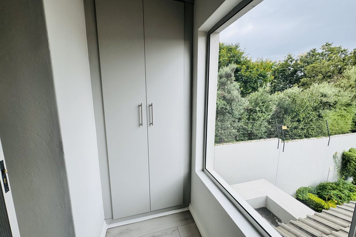 A bright, empty bedroom featuring modern built-in cupboards, light laminate flooring, and a large window overlooking the garden.