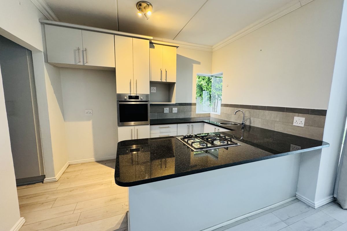 Modern kitchen featuring granite countertops, built-in oven, gas hob, and ample cabinetry, finished with light laminate flooring and a neutral tiled backsplash.