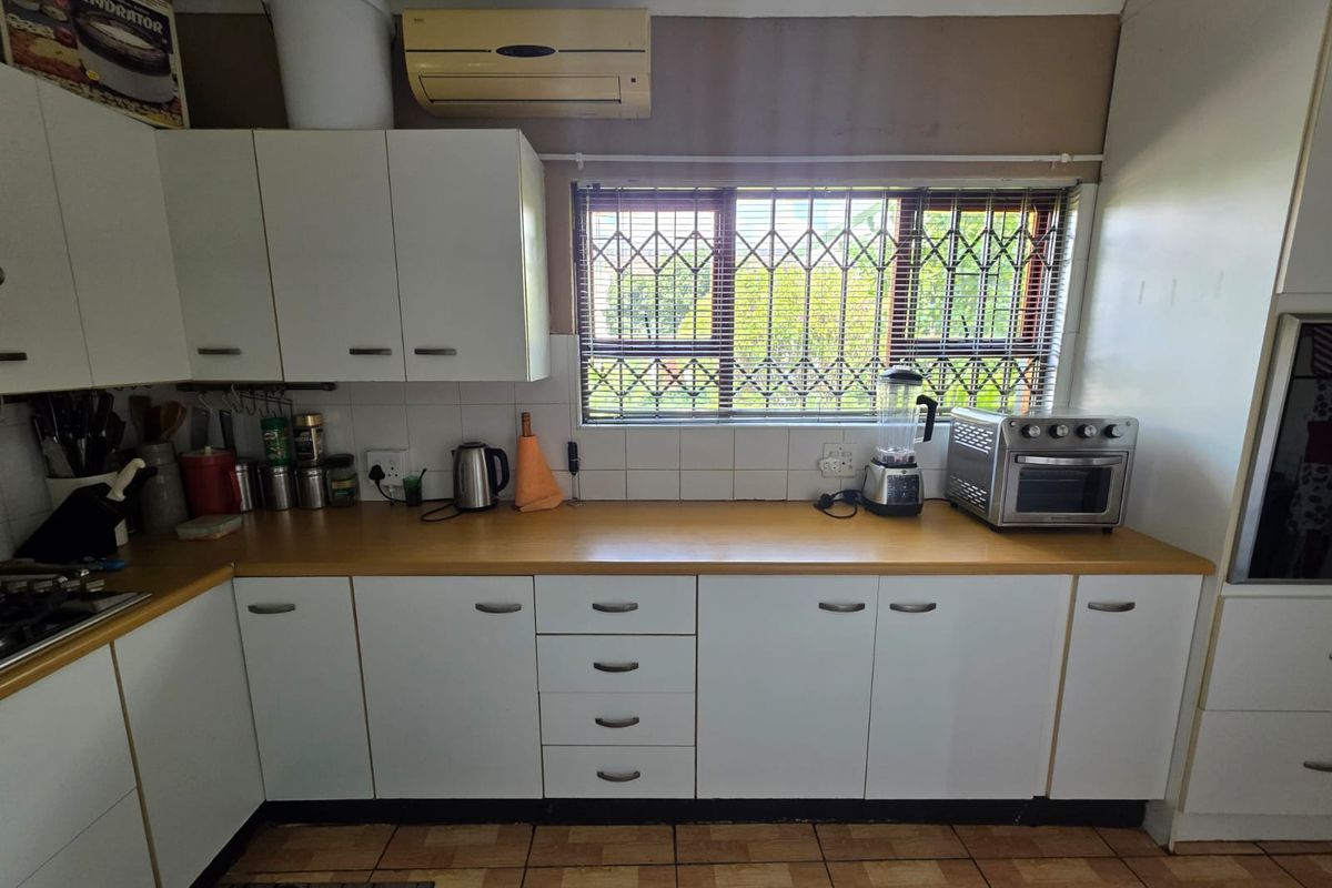 A functional kitchen featuring white cabinetry, laminate countertops, tiled flooring, and a wall-mounted air conditioning unit, providing a practical workspace with natural light.