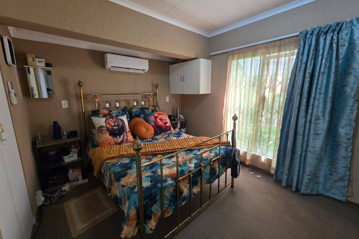 A bedroom featuring a split-system air conditioner, built-in wall cabinetry, and a sliding glass door with security gate leading to the exterior.