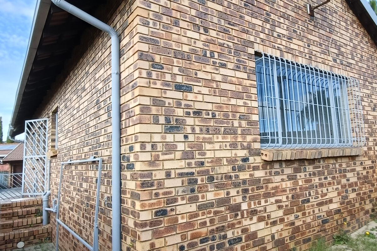 Exterior view of the townhouse featuring face-brick facade, security bars on windows, and a paved side walkway.