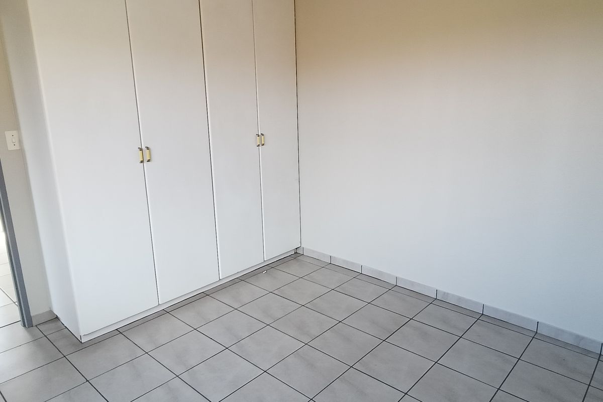 A bright, empty bedroom featuring built-in cupboards, tiled flooring, and direct access to an adjacent bathroom.