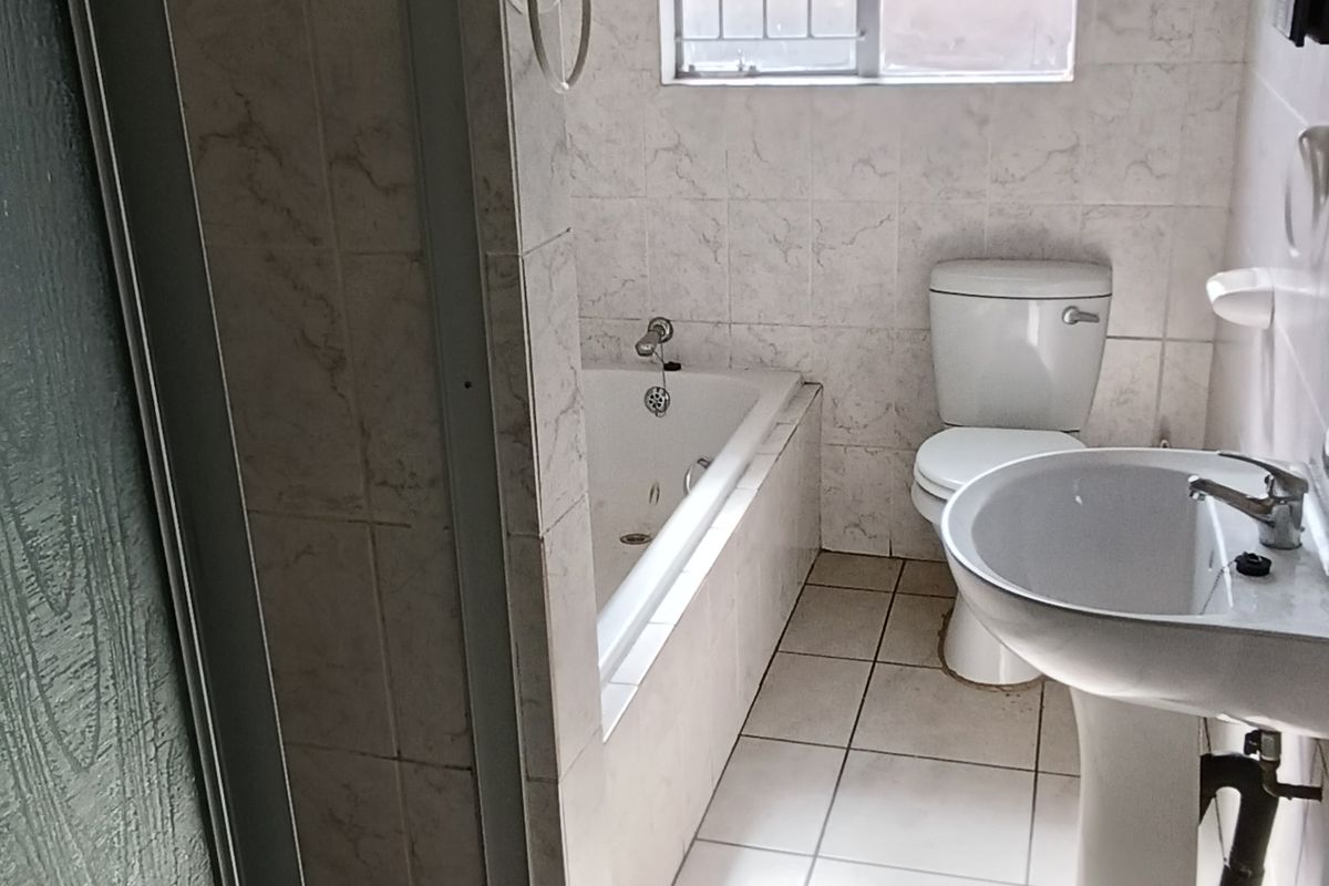 A functional bathroom featuring a shower enclosure, a built-in bathtub, a pedestal basin, and a toilet with tiled flooring and wall accents.