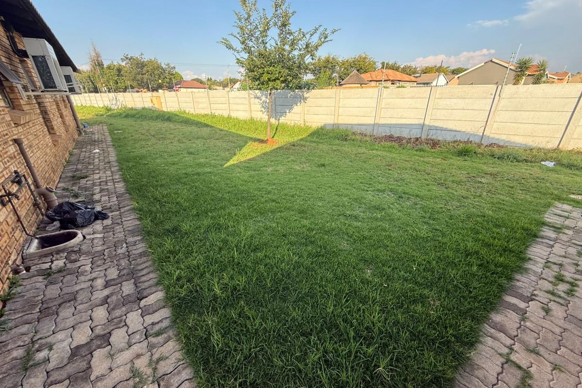 A spacious rear garden featuring a lawn area, paved walkway, and perimeter concrete walling.