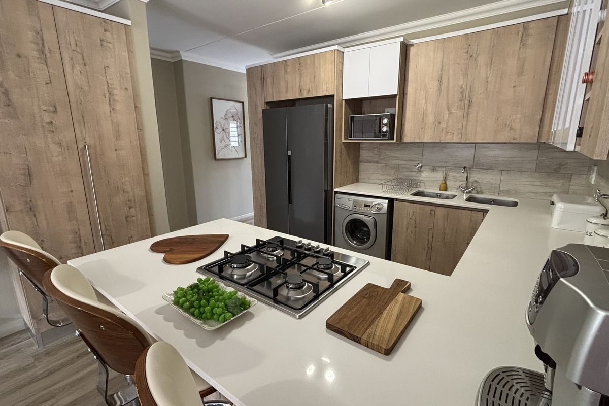 Modern kitchen featuring wood-grain cabinetry, stone countertops, a built-in gas hob, and integrated laundry appliances.
