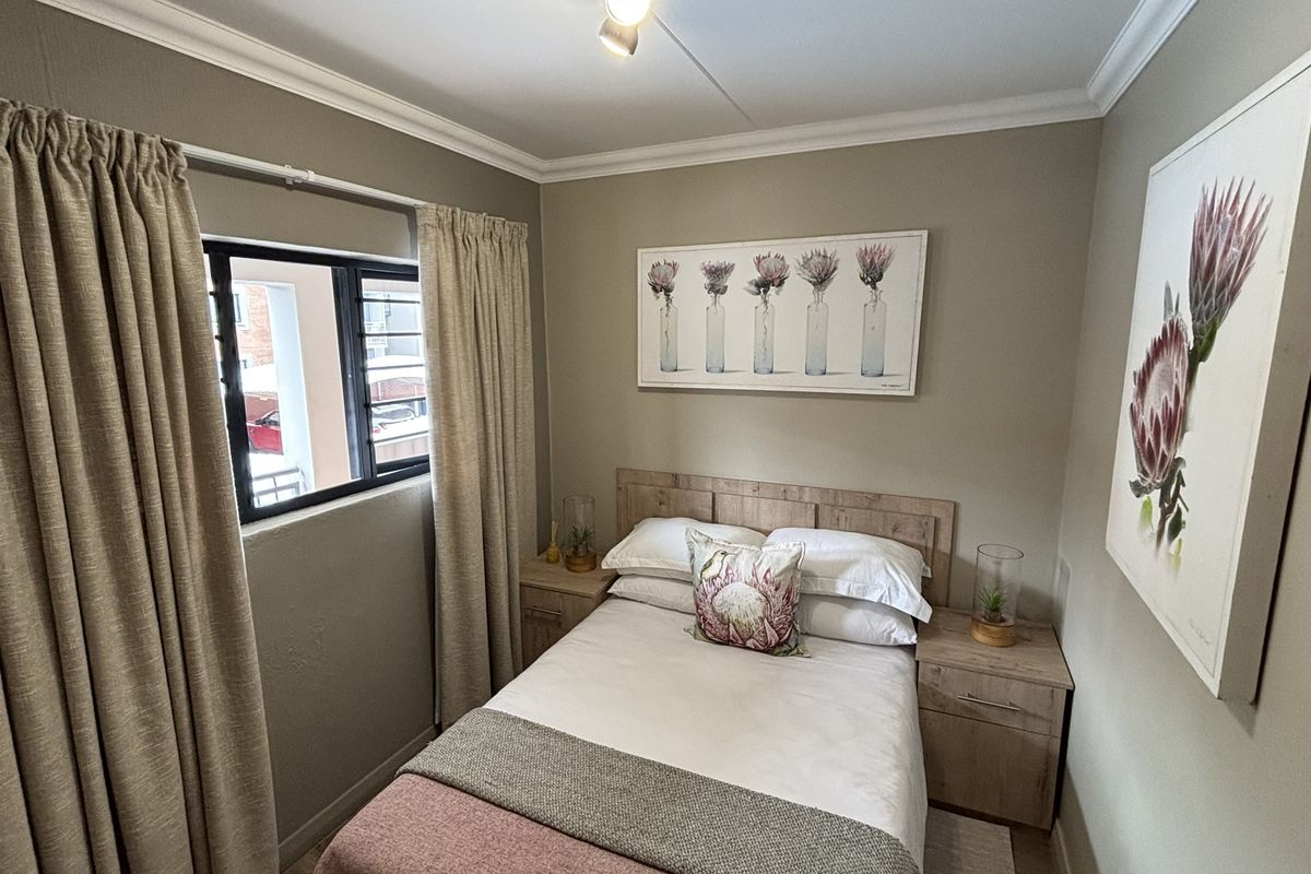 A cozy bedroom featuring neutral wall tones, a window with curtain tracks, and crown molding, providing a comfortable and well-maintained living space.