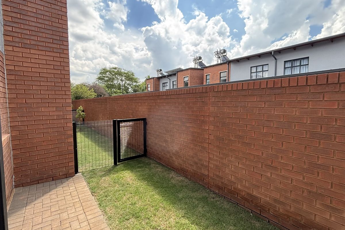 A private rear garden area featuring a paved patio, a small lawn, and a secure perimeter brick wall.