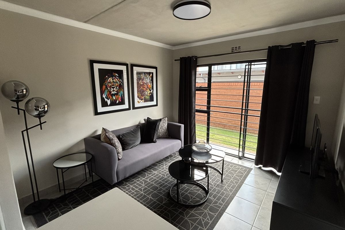 A comfortable living room featuring tiled flooring, neutral wall tones, and a large sliding glass door providing access to the outdoor area.