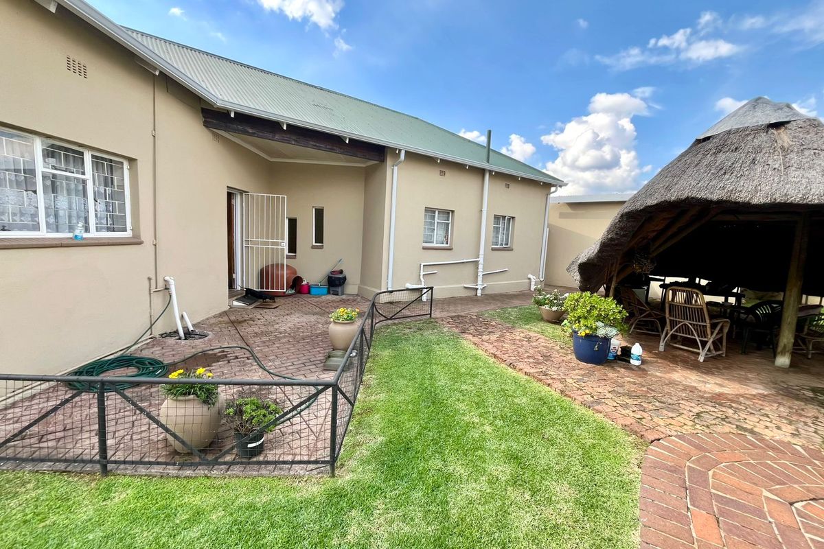 Rear view of the property featuring a paved patio area, a thatched lapa, and a well-maintained lawn.