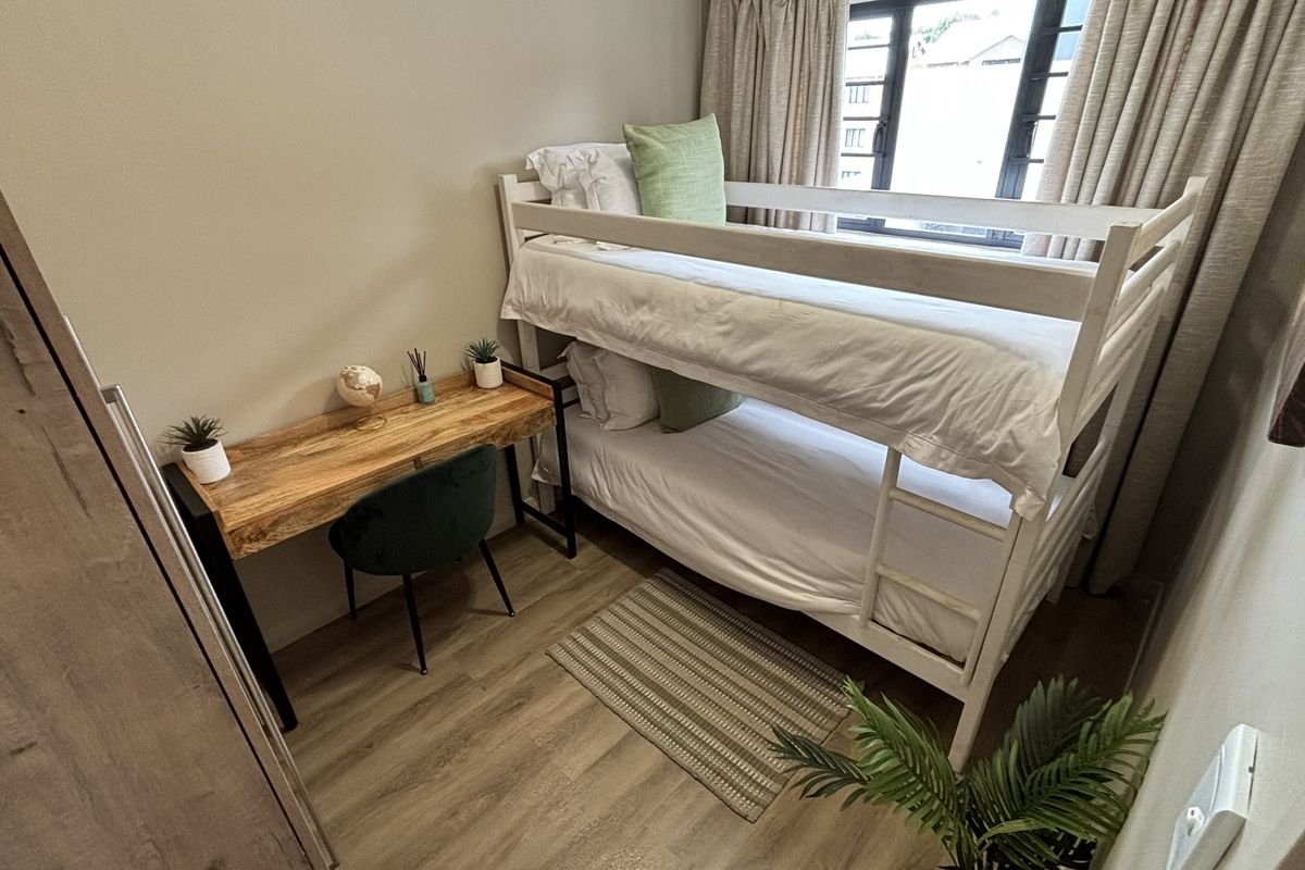 A compact bedroom featuring wood-look flooring, built-in cabinetry, and a window with curtains, providing a functional and well-maintained living space.