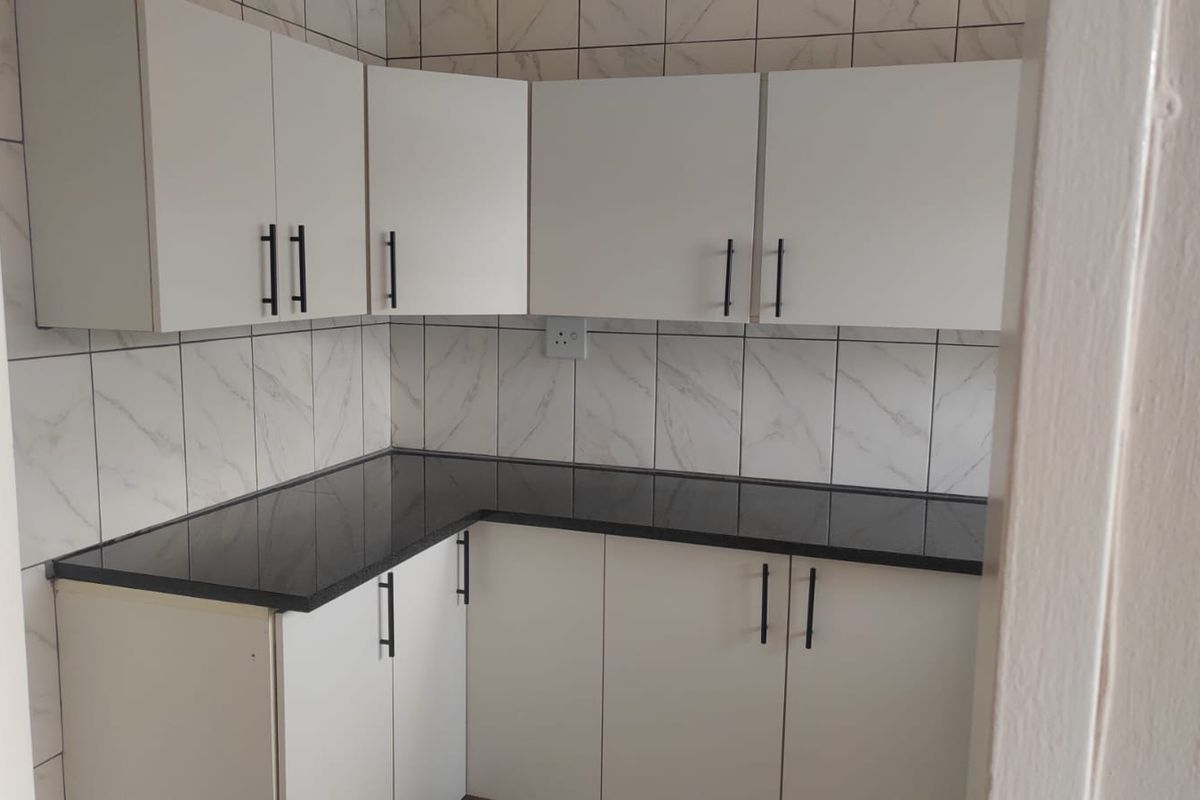 A compact, modern kitchen featuring white cabinetry, dark countertops, and marble-effect tiled splashbacks.